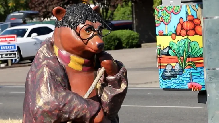 Colorfully painted bear statue wearing glasses and a scarf displayed during a community BearFest public art event.