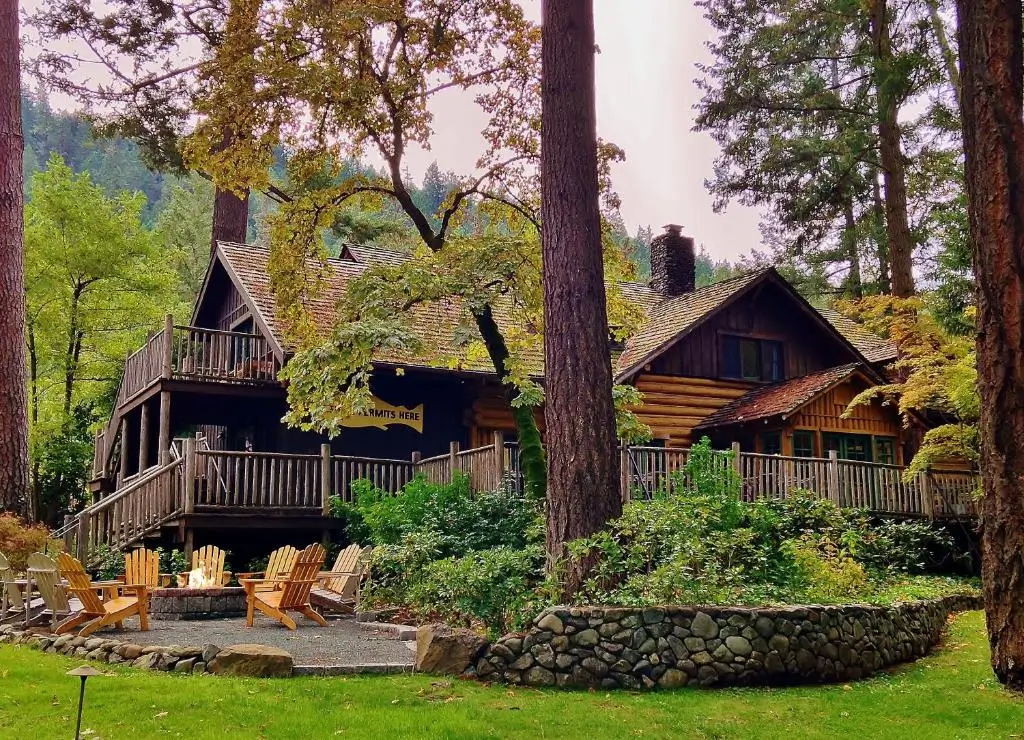 Rustic woodland lodge surrounded by towering trees with a fire pit and Adirondack chairs creating a cozy outdoor gathering space.